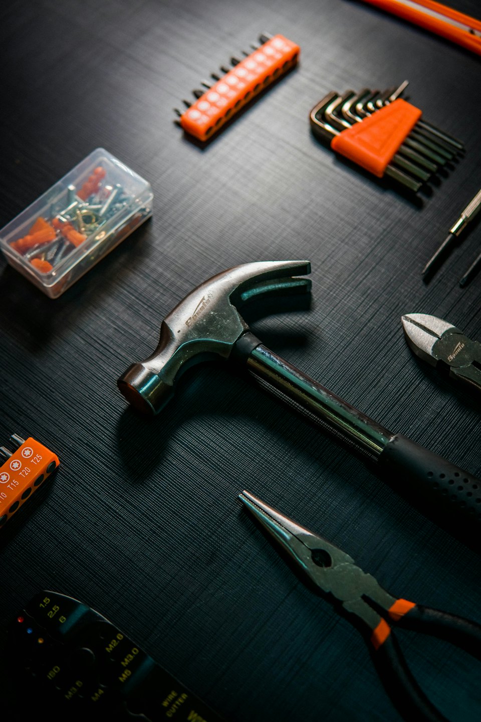 Verschiedene Handwerkzeuge und Baumaterialien auf dunklem Untergrund ausgebreitet.
